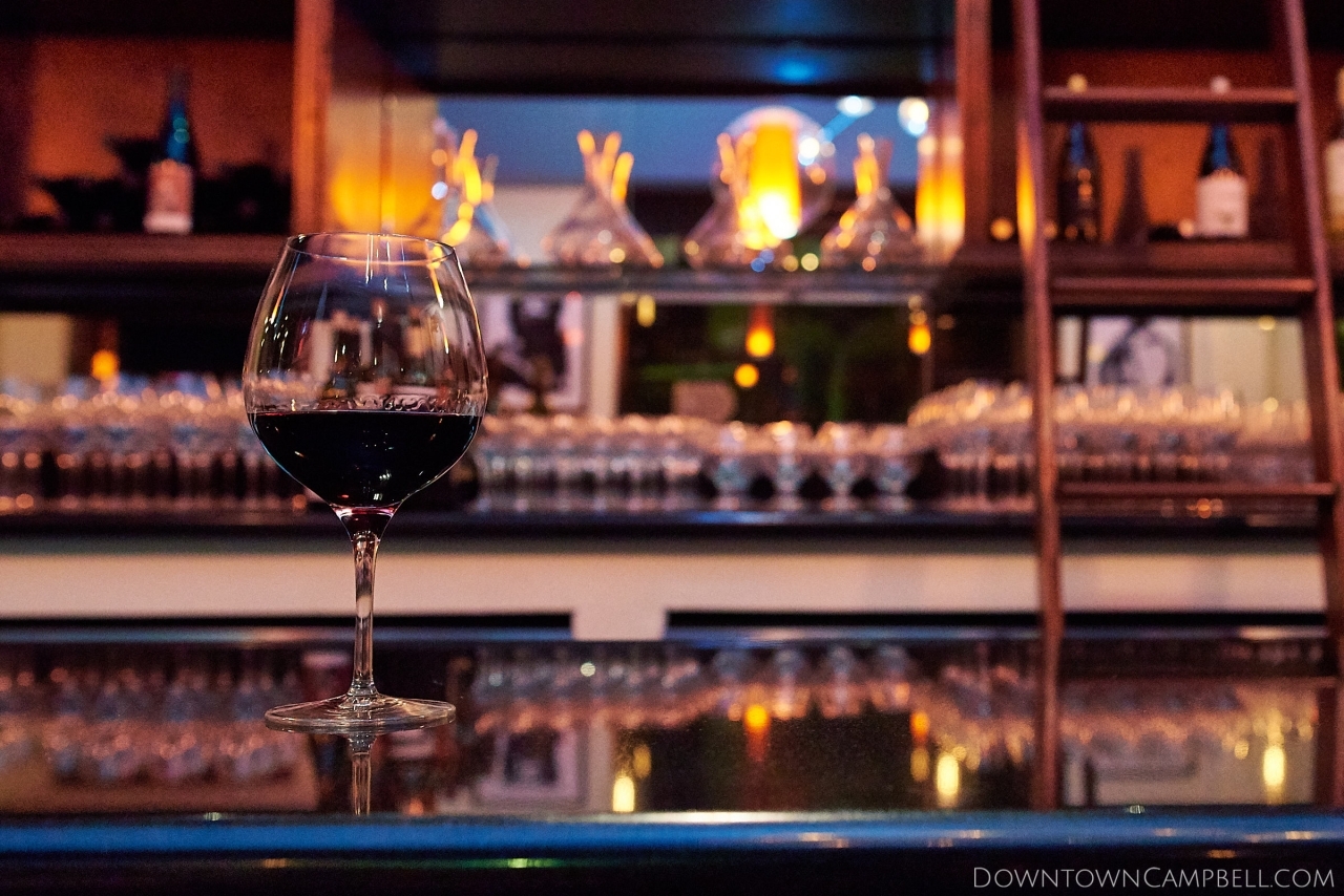 Wine Glass on Wine Bar Large wine glass filled with red wine sitting alone on a wine bar with a wine library in the background.